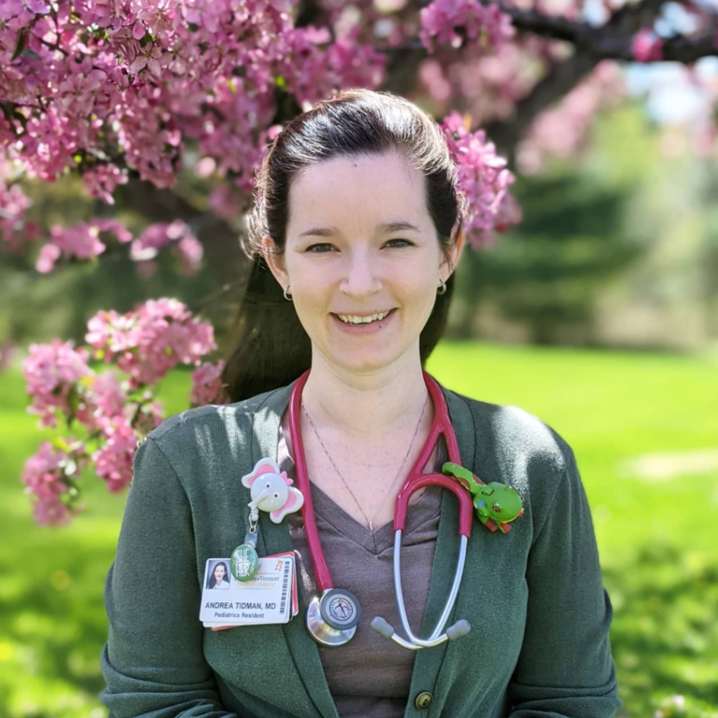 A woman with a stethoscope standing in front of a blossoming tree.