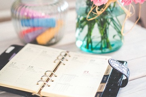 A daily planner open on a table near some colorful jars and vases.